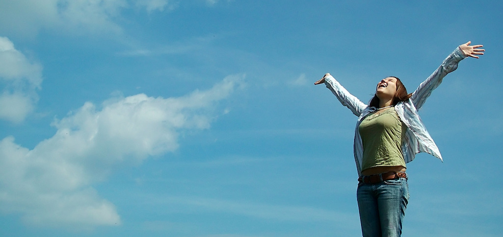 Unha muller cos seus brazos abertos frente a un ceo azul. Foto de Jess Hall.